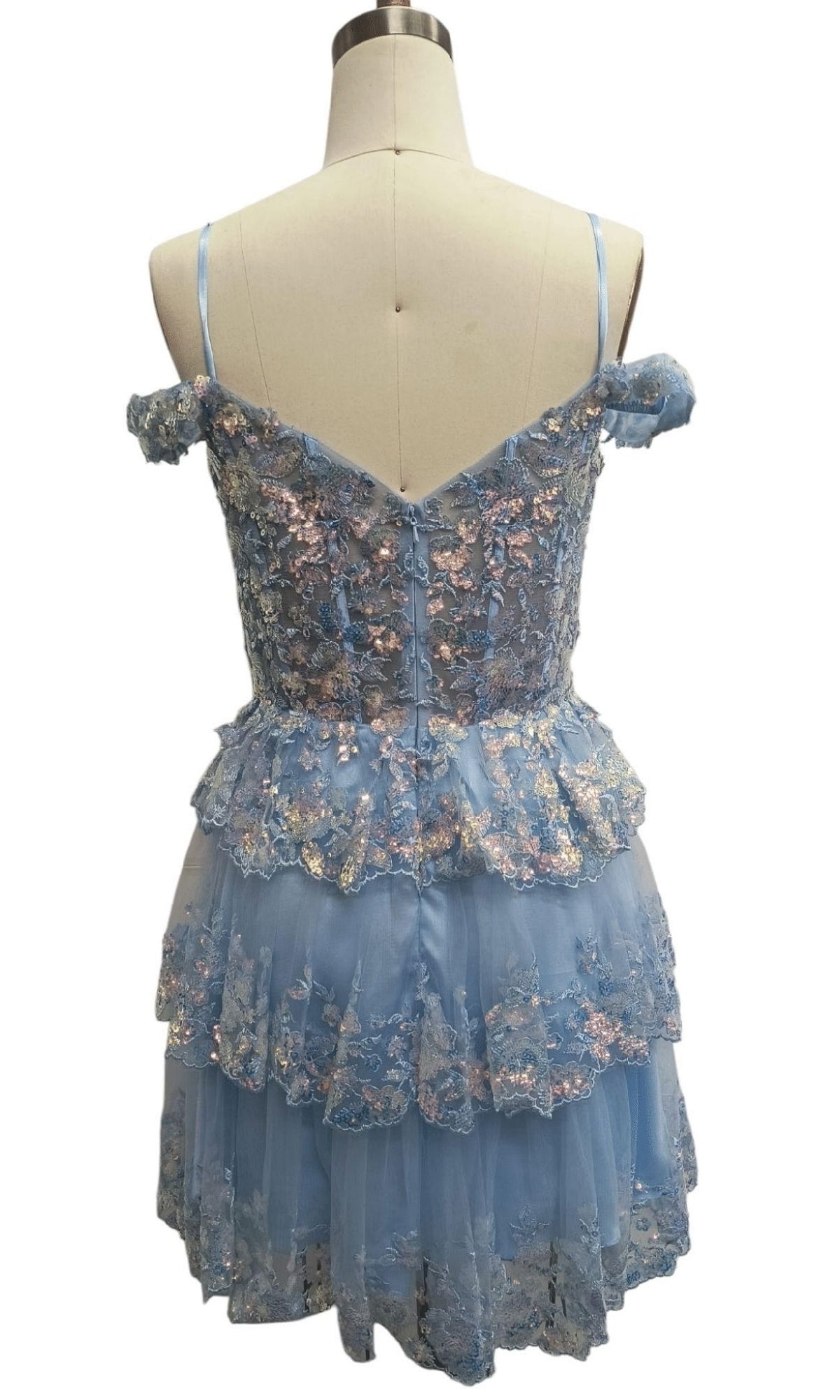 Back view of a mannequin wearing the Dave & Johnny 12418 short blue homecoming dress featuring off-shoulder tiered lace, floral embroidery, a corset bodice, and delicate spaghetti straps.